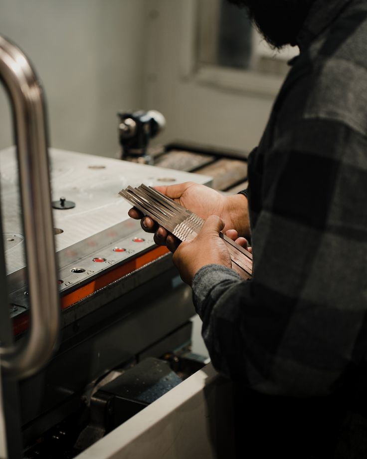 Technician holding machined metal parts beside a machine for inspection